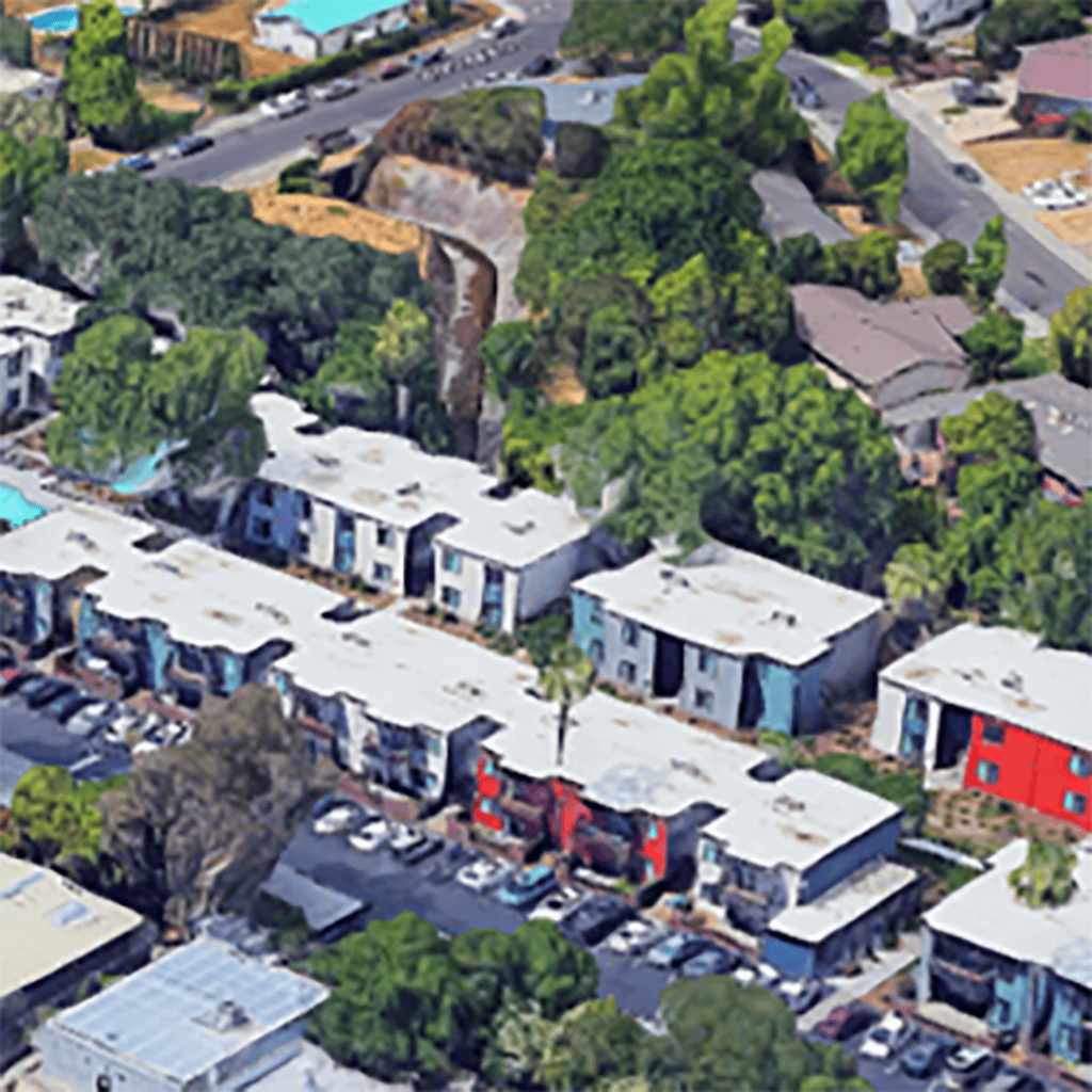 Aerial view of a residential area with modern boxy houses, dense greenery, and a parking lot, with a distinct red-roofed building amidst the gray and blue rooftops.
