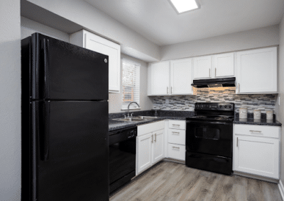 Modern kitchen interior with white cabinetry, black appliances, multicolored backsplash, and granite countertops. the room has bright lighting and wood-style flooring.