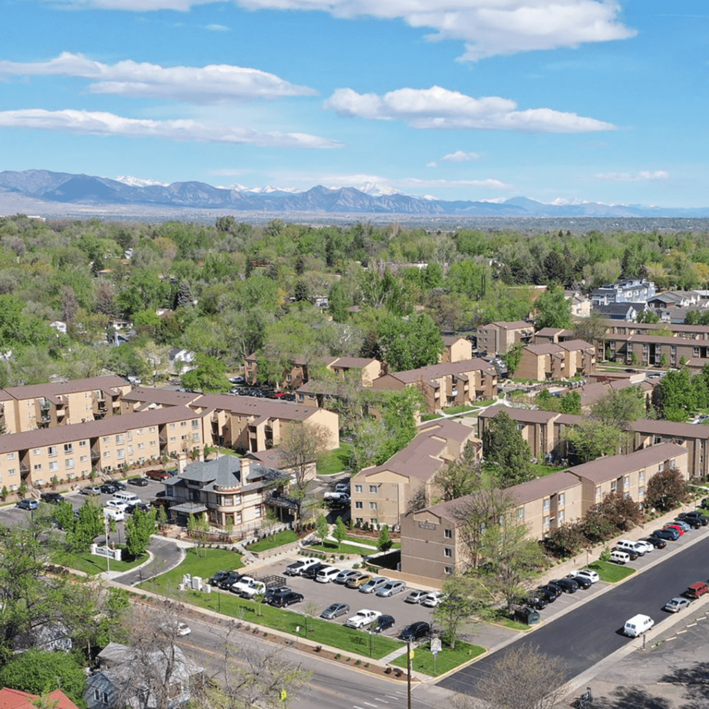 Aerial view of a residential area with multiple apartment buildings surrounded by lush greenery and a mountain range in the background under a clear blue sky.