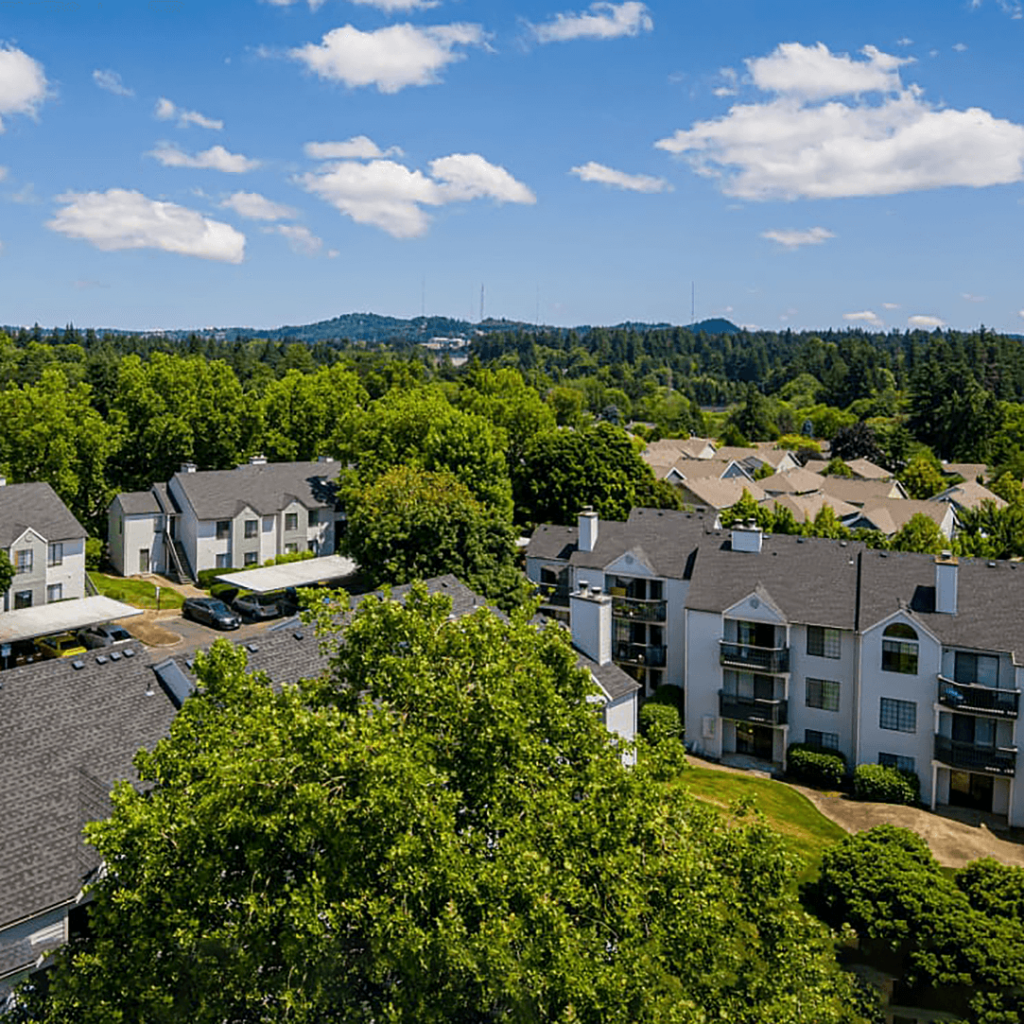 Aerial view of a residential neighborhood with multi-story apartment buildings surrounded by lush green trees under a clear blue sky.